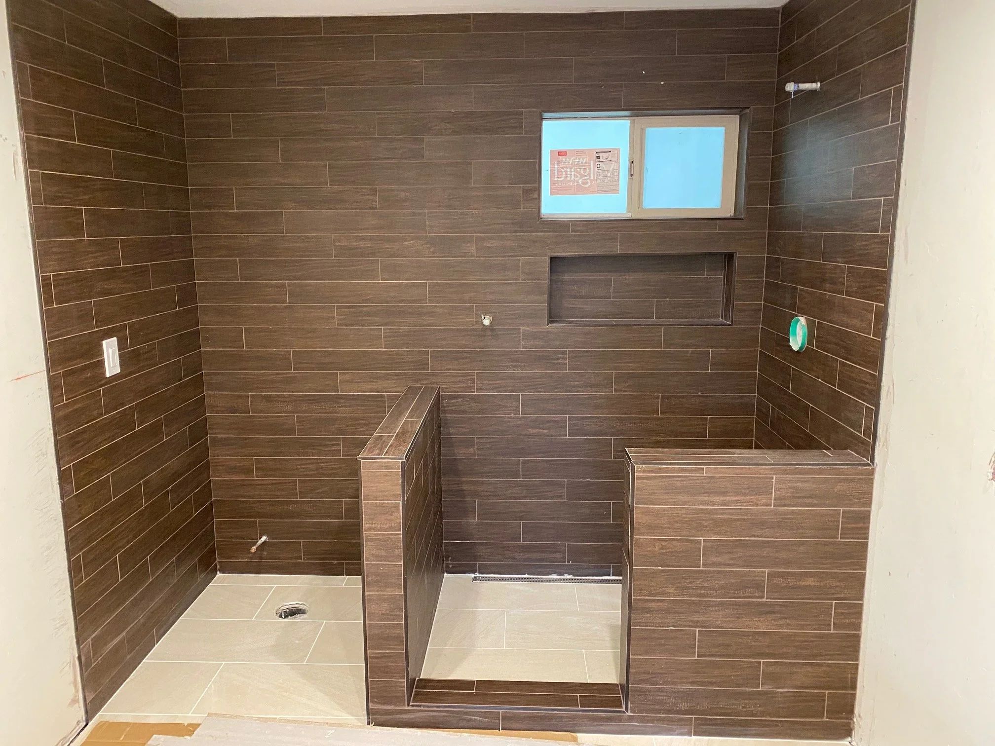 Walk-in shower under construction, with wood-look wall tile, a built-in bench and a tiled niche set into the wall.